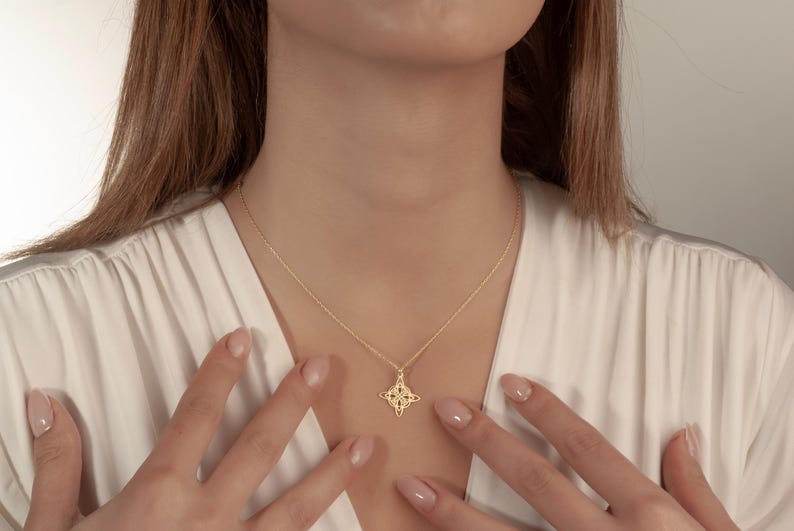 Pu&ograve; includere: Una collana color oro con un ciondolo a forma di stella a quattro punte. La collana &egrave; indossata da una persona che indossa un top bianco. Il ciondolo ha un design traforato. La catena della collana &egrave; delicata.