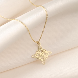 Pu&ograve; includere: Una collana con pendente dorato con un design a nodo a quattro punte. Il pendente &egrave; appeso a una delicata catena, su uno sfondo di morbido tessuto bianco sporco. La collana &egrave; un gioiello.