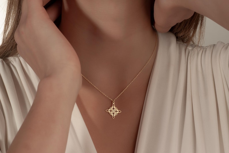 Pu&ograve; includere: Una collana con pendente color oro con un design a nodo celtico. La collana &egrave; indossata da una persona con un top color crema. Il pendente &egrave; un design dettagliato e traforato, sospeso a una delicata catena.