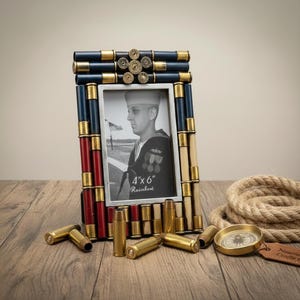 May include: A rectangular photo frame with a black and white image of a sailor. The frame is decorated with brass bullet casings and painted in red, white, and blue. The photo is 4" x 6".