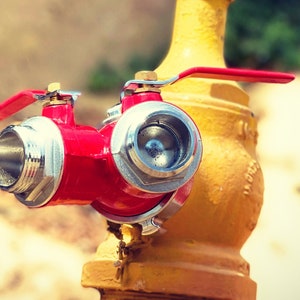 May include: A red fire hydrant with two valves, one with a lever handle and the other with a wheel handle. The hydrant is attached to a yellow pipe.