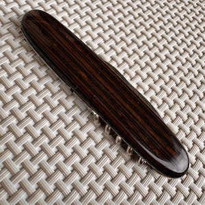 Puede incluir: Un cuchillo de bolsillo cerrado con un mango de madera oscura y detalles plateados. El mango tiene un patrón de rayas.