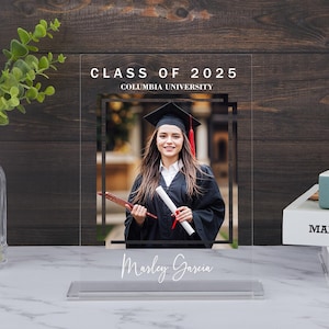 May include: A clear acrylic photo frame with a black border and a white background. The frame has a photo of a woman in a graduation cap and gown holding a diploma. The text "CLASS OF 2025 COLUMBIA UNIVERSITY" is printed at the top of the frame. The text "Marley Garcia" is printed at the bottom of the frame.
