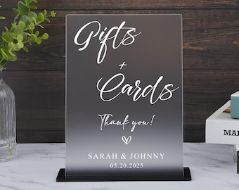 Op de afbeelding: Een rechthoekig bord van mat acryl op een zwarte voet met witte tekst die Gifts + Cards, Thank you! leest, een klein hartsymbool, en de namen Sarah & Johnny met de datum 20-05-2025 gedrukt in een strak, modern schreefloos lettertype.