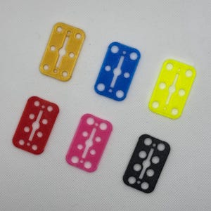 Puede incluir: Seis llaveros de plástico con forma de hoja de afeitar en diferentes colores: amarillo, azul, rojo, rosa, negro y verde. Cada llavero tiene una ranura en el medio y cinco agujeros alrededor de los bordes.