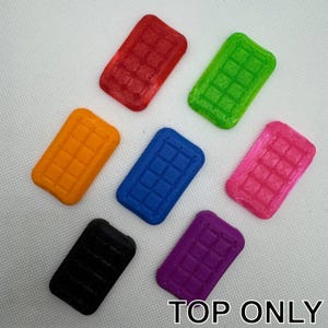 Puede incluir: Siete pequeñas baldosas rectangulares con un patrón de cuadrícula, cada una en un color diferente: rojo, naranja, amarillo, azul, rosa, morado y negro. Las baldosas están dispuestas en un semicírculo con el texto "TOP ONLY" en la parte inferior.