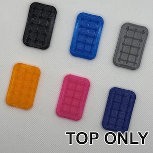 Puede incluir: Seis baldosas de plástico de diferentes colores con un patrón de cuadrícula. Las baldosas son negras, azules, grises, naranjas, rosas y azul oscuro. Las baldosas están dispuestas en semicírculo sobre una superficie blanca. El texto "TOP ONLY" está impreso en negro en la parte inferior de la imagen.