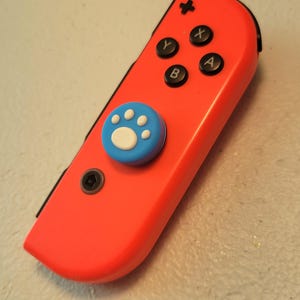 May include: A bright red Nintendo Switch Joy-Con controller with a blue paw print button cap.