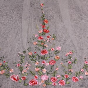 May include: A sheer, white veil with an embroidered floral design. The embroidery features red, pink, and peach-colored roses with green leaves. The flowers are arranged in a delicate pattern across the veil, suitable for bridal wear.