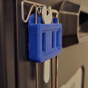 Può includere: Un portautensili stampato in 3D blu con una chiave inglese in metallo attaccata. Il supporto è montato su una superficie nera.