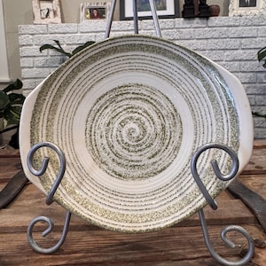 May include: A white ceramic serving dish with a green swirl pattern. The dish is on a metal stand.