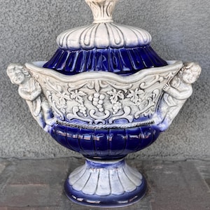 May include: A white and blue ceramic serving dish with a lid. The dish has a decorative design of grapes and leaves. The lid has a knob in the shape of a flower.