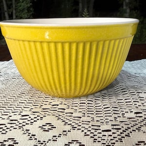 May include: A bright yellow ceramic mixing bowl with vertical ribbed detailing. The bowl has a wide rim and a white interior. This kitchenware item is suitable for baking and food preparation.