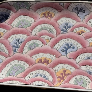 May include: A rectangular ceramic serving dish with a pink and white floral design. The dish features a repeating pattern of stylized flowers with white outlines and details in shades of green, blue, and orange.
