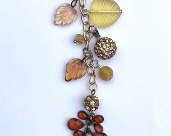 May include: A gold-toned keychain with a lobster clasp, adorned with various charms. These include amber-colored leaf-shaped beads, a cluster of orange teardrop-shaped beads, and a gold-colored rhinestone ball.