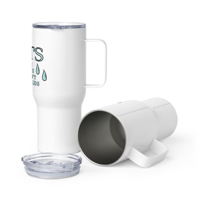 May include: White stainless steel travel mug with a black handle and a lid. The mug features a graphic of a teardrop with the text "It's the tough times that don't break you".