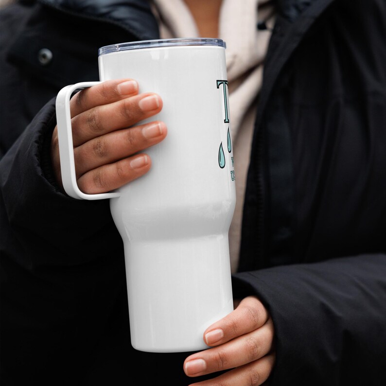 May include: White stainless steel travel mug with a black handle. The mug features a blue and white graphic that says "Tears of a Unicorn".