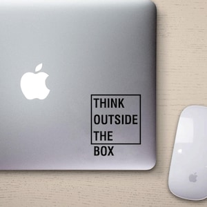 Könnte beinhalten: Ein silberner Laptop mit einem weißen Apple-Logo und einem schwarzen Aufkleber mit der Aufschrift "Think Outside The Box" in der oberen rechten Ecke.