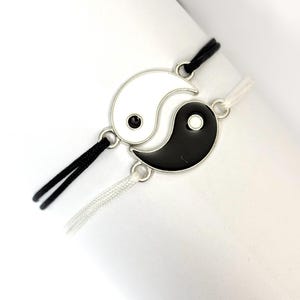 Könnte beinhalten: Zwei passende Armbänder mit Yin-und-Yang-Design. Ein Armband hat einen schwarz-weißen Yin-Yang-Anhänger mit schwarzem Kordel, das andere einen weiß-schwarzen Yin-Yang-Anhänger mit weißem Kordel.