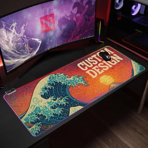 Peut inclure: Un grand tapis de souris rectangulaire avec un motif coloré représentant une grande vague, une montagne et un soleil. Le tapis de souris a un fond rouge, orange et jaune vif avec une vague bleue et blanche. Le texte "CUSTOM DESIGN" est imprimé en blanc sur le tapis de souris.