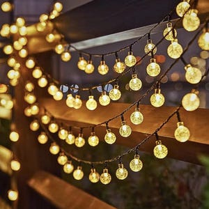 May include: A string of solar powered globe lights with a warm white glow. The lights are strung on a black wire and are ideal for decorating a patio or garden.