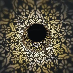 Puede incluir: Una linterna de metal decorativa con un intrincado patrón floral. La linterna está iluminada desde el interior, proyectando un cálido resplandor a través de los recortes.