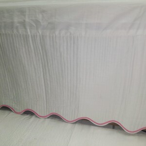 May include: White bed skirt with a pink scalloped edge.