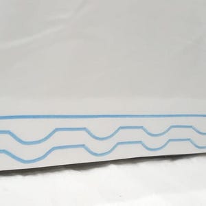 Könnte beinhalten: Weißer Stoff mit einem blauen, wellenförmigen Saum am unteren Rand.