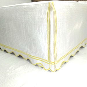 May include: White bed skirt with a scalloped edge and yellow trim.