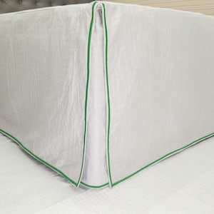 Puede incluir: Falda de cama blanca con ribete verde alrededor de los bordes. La falda está hecha de una tela suave y sedosa.