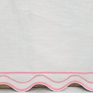 以下が含まれることがあります： ピンクのフリルが付いた白い生地。フリルにはピンクのステッチが2列あります。
