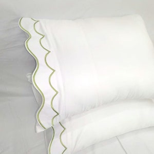 Puede incluir: Dos fundas de almohada blancas con un ribete festoneado verde. Las fundas de almohada están hechas de una tela suave y cómoda.