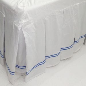 May include: White bed skirt with blue stripes around the bottom edge. The skirt is pleated and has a smooth, silky texture.