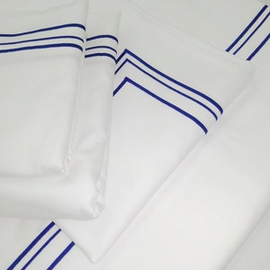 May include: White bed sheets with blue trim. The sheets are folded and stacked on top of each other.