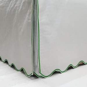 May include: A white bed skirt with a scalloped edge and a green trim.