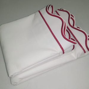 Puede incluir: Sábanas blancas de cama con un borde festoneado y un ribete rojo.