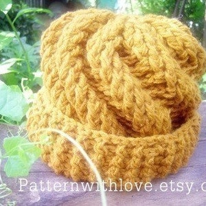 Puede incluir: Un gorro de punto de color amarillo mostaza con un patrón de trenza. El gorro está hecho con un hilo grueso y tiene un ala ancha.