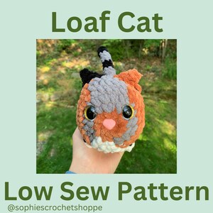 May include: A crocheted cat toy in the shape of a loaf of bread. The cat is grey, orange, and black with large, black eyes. The toy is being held in a hand. The text "Loaf Cat" and "Low Sew Pattern" is visible in the image. The text "@sophiescrotchetshoppe" is also visible in the image.