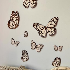 Op de afbeelding: Een verzameling houten vlinder wanddecoraties in verschillende maten. De vlinders zijn bruin met crèmekleurige details, wat een natuurlijke en decoratieve uitstraling creëert. Ze zijn gemonteerd op een lichtblauwe muur, wat wijst op een kinderkamer.