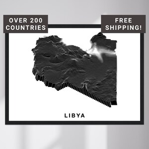 May include: Black and white topographic map of Libya, framed in black. The map is a detailed representation of the country's terrain, with contour lines creating a 3D effect. Text at the top reads "OVER 200 COUNTRIES" and "FREE SHIPPING!" at the top. The name "LIBYA" is at the bottom.