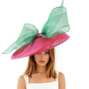 Puede incluir: Un sombrero de ala ancha con un gran lazo decorativo. El sombrero presenta una base rosa brillante y un lazo verde esmeralda transparente. Un accesorio llamativo, perfecto para eventos especiales.
