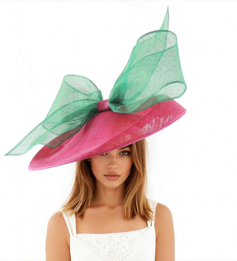 Puede incluir: Un sombrero de ala ancha con un gran lazo decorativo. El sombrero presenta una base rosa brillante y un lazo verde esmeralda transparente. Un accesorio llamativo, perfecto para eventos especiales.