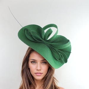 May include: A large, green, wide-brimmed hat with a large bow on top. The hat is made of a woven material and has a slightly textured surface.