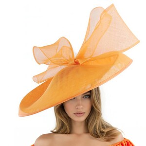 Puede incluir: Un sombrero naranja vibrante con ala ancha y un gran lazo. El sombrero est&aacute; hecho de una tela fina y ligera. El sombrero es una pieza llamativa, perfecta para ocasiones especiales.