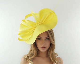 May include: A vibrant yellow hat featuring a large, sculpted bow design. The hat is crafted from woven fabric and has a gently curved brim. A single, slender yellow feather is attached. A fashionable headpiece.