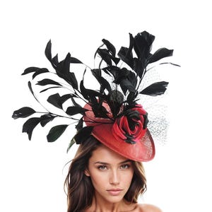 May include: A red hat with a black rose and black feathers. The hat has a wide brim and is decorated with a large, red rose and black feathers. The hat is likely for a special occasion.