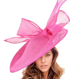 May include: A large, bright pink hat with a wide brim and a large bow. The hat is made of a delicate, woven material.