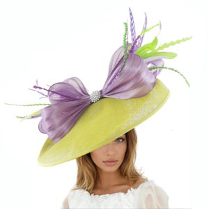 May include: A wide-brimmed, lime green hat with a large, lavender bow and a sparkling rhinestone embellishment. The hat is adorned with green and purple feathers, creating a stylish and elegant accessory.