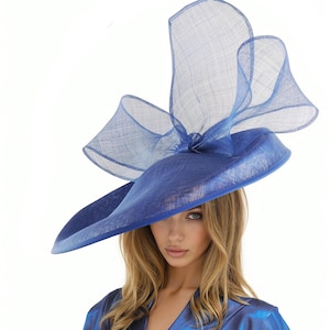 Puede incluir: Un llamativo sombrero azul con ala ancha y un acento fluido y transparente. El dise&ntilde;o del sombrero presenta una base estructurada y una parte superior delicada y aireada, creando un look dram&aacute;tico y elegante. Un accesorio de moda llamativo.