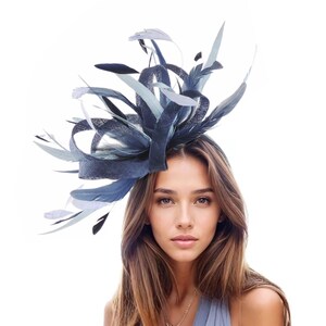 May include: A navy blue and light blue feather fascinator. The headpiece features a woven base with looping fabric and a variety of feathers in shades of blue and gray. The accessory is designed to be worn on the head.